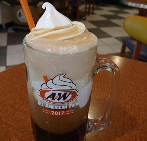 A frosty mug of root beer float topped with creamy soft serve ice cream, set on a wooden table in a diner.