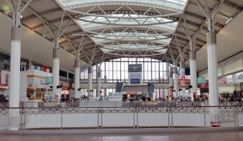 A spacious indoor shopping area with high ceilings, food stalls, and a large window letting in natural light.