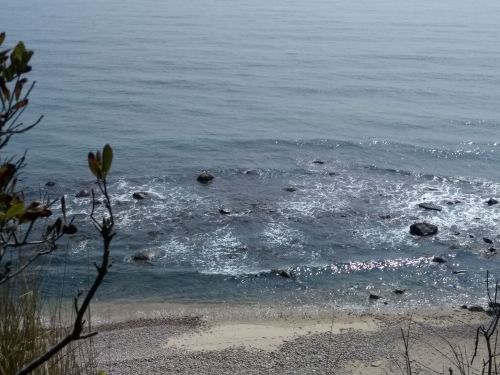 A serene coastal view with gentle waves, rocky shoreline, and a calm sea under a hazy sky.