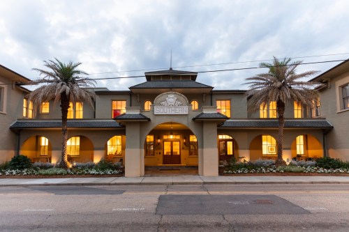Historic building with palm trees, warm lights in windows, and a sign reading "Southern" under a cloudy sky.