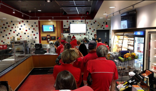 A line of people in red shirts waiting to order at a fast-food restaurant with colorful decor.