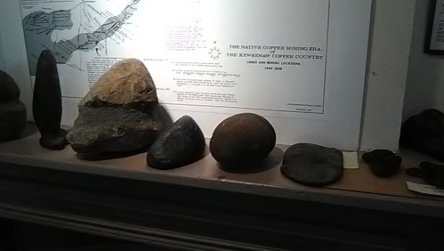 A display of various rocks and minerals on a shelf, with a map in the background detailing copper mining areas.