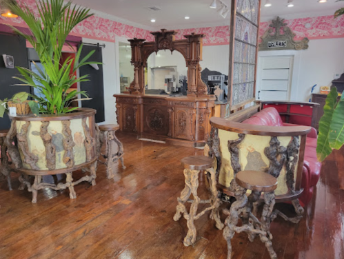 A cozy interior featuring ornate wooden furniture, a bar, and lush plants in a vibrant, stylish setting.