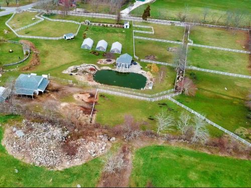 Aerial view of a green landscape featuring a pond, several outbuildings, and white fencing.