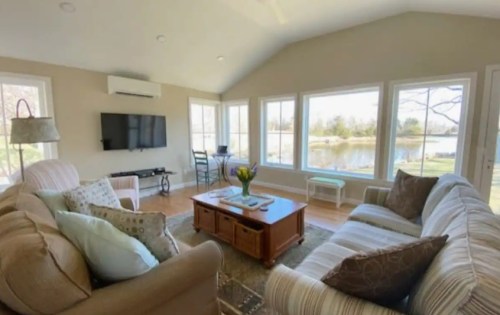 Cozy living room with large windows overlooking a lake, featuring a sofa, coffee table, and a TV.