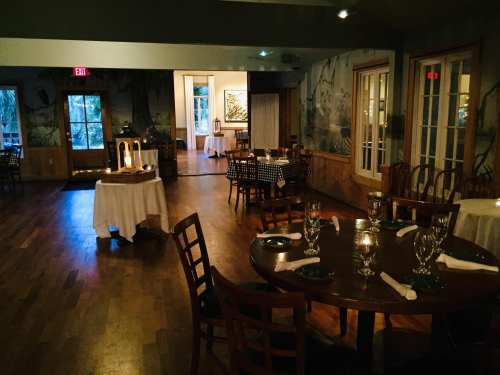 Cozy restaurant interior with wooden floors, tables set for dining, and soft lighting creating a warm atmosphere.