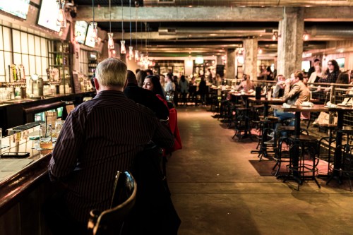 A bustling bar scene with patrons seated at the counter and tables, warm lighting, and a lively atmosphere.