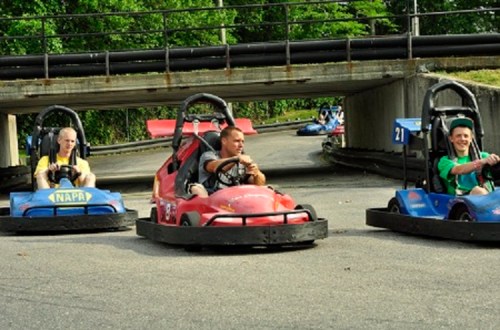 Three go-karts on a track, with drivers focused and ready to race in a green outdoor setting.