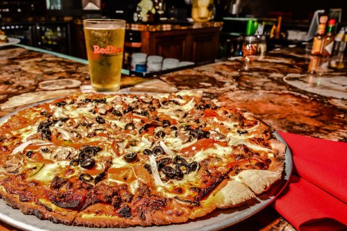A delicious pizza topped with pepperoni, mushrooms, and olives, served on a silver platter with a pint of beer in the background.