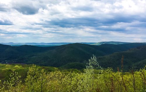 A panoramic view of rolling green hills under a cloudy sky, with distant mountains in the background.
