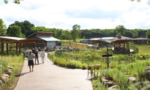 A scenic outdoor area with people walking along a path, surrounded by greenery and modern buildings in the background.