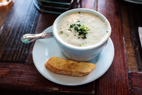 A bowl of creamy soup garnished with herbs, served on a plate with a small piece of bread.