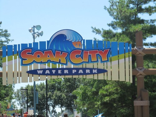 Sign for Soak City Water Park featuring a wave graphic and surrounded by trees on a sunny day.