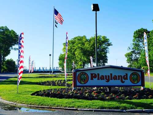 A colorful sign for Playland, surrounded by flags and greenery, with a clear blue sky in the background.