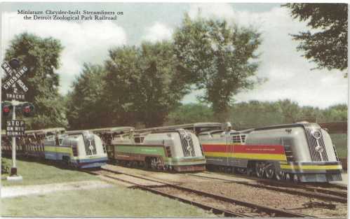 Colorful miniature trains lined up on tracks at the Detroit Zoological Park Railroad, surrounded by trees.