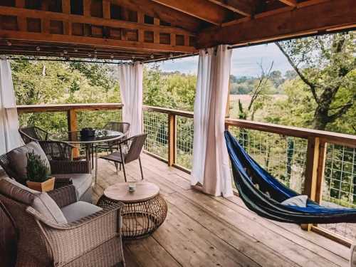 A cozy outdoor deck with a table, chairs, and a hammock, surrounded by trees and a scenic view.