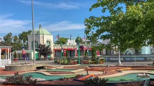 A colorful mini-golf course with decorative buildings and trees under a clear blue sky.