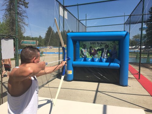 A person aiming an arrow at an inflatable archery target in a sunny outdoor setting.