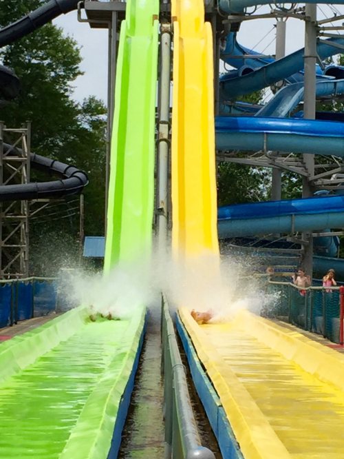 Two water slides in bright green and yellow, with splashes as riders descend into a pool below.