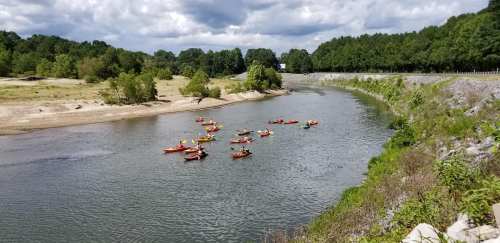 A group of kayakers paddles along a winding river surrounded by lush greenery and a cloudy sky.