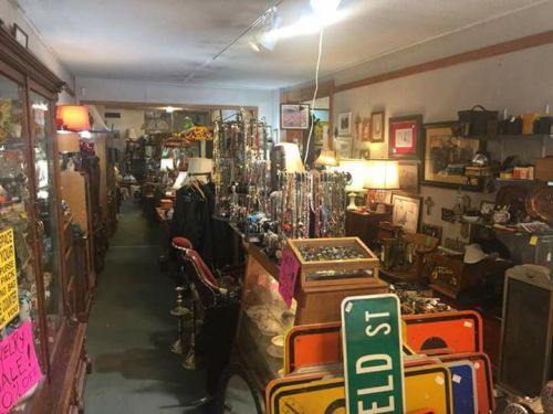 A cluttered antique shop filled with various items, including jewelry, furniture, and vintage signs.