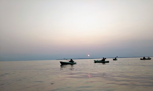 Silhouettes of kayakers on calm water at sunset, with a soft gradient sky in the background.