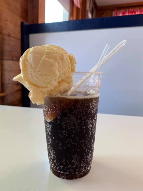 A clear cup filled with dark soda topped with a scoop of vanilla ice cream and two plastic straws.
