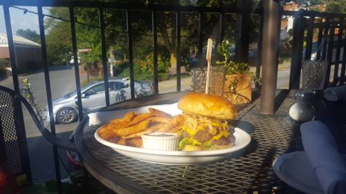 A burger with melted cheese and onions, served with fries and dipping sauce, on a table outdoors.