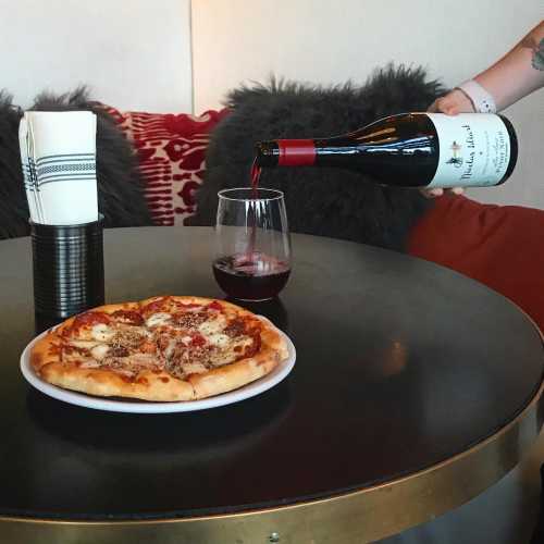 A cozy setting with a pizza, a glass of red wine being poured, and a plush sofa in the background.