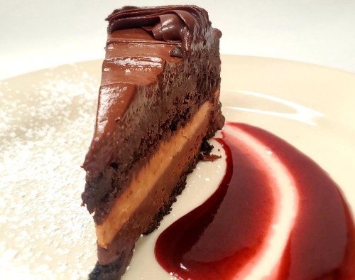 A slice of rich chocolate cake with a creamy filling, drizzled with berry sauce and dusted with powdered sugar.