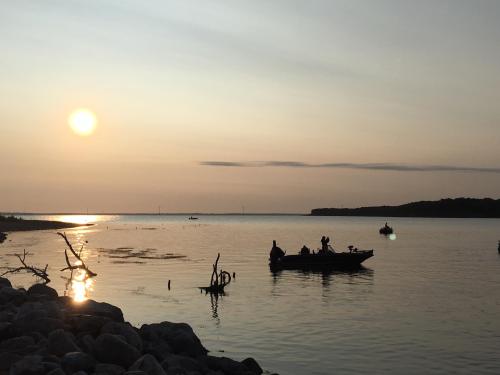 Silhouetted boats on a calm lake at sunset, with the sun reflecting on the water and trees in the foreground.