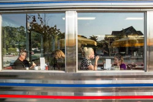 A diner scene through a window, showing people enjoying meals and conversation inside.