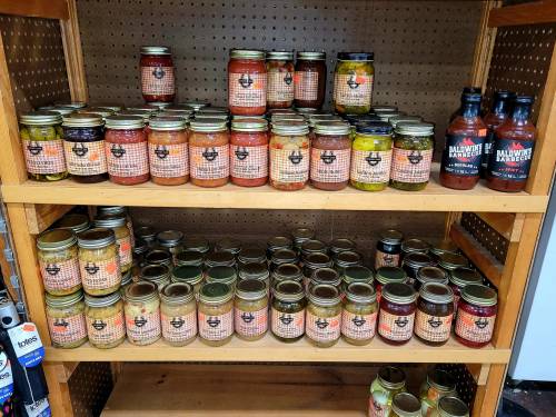 A wooden shelf displaying various jars of sauces and pickled items, all labeled with a distinctive logo.