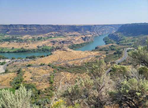 A scenic view of a winding river surrounded by rocky cliffs and dry vegetation under a clear blue sky.