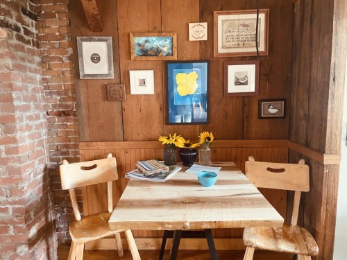 Cozy dining nook with a wooden table, two chairs, sunflowers, and framed art on the walls.
