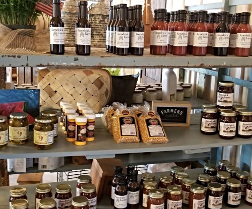 Shelves filled with various jars and bottles of sauces, preserves, and condiments in a rustic market setting.