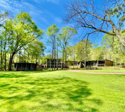 A sunny landscape featuring modern buildings surrounded by lush green trees and a vibrant lawn.