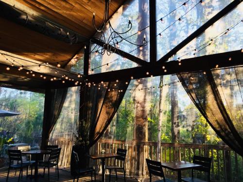 Cozy indoor space with wooden beams, string lights, and sheer curtains, surrounded by greenery.