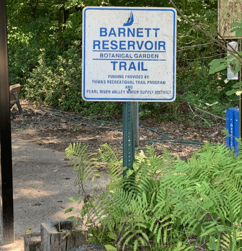 Sign for Barnett Reservoir Botanical Garden Trail, with information about funding and local water district. Surrounded by greenery.