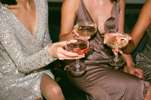 Three people in elegant dresses toast with champagne glasses, celebrating in a cozy setting.