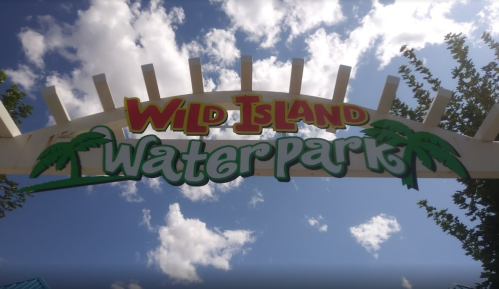 Sign for Wild Island Water Park with palm trees, under a blue sky with clouds.