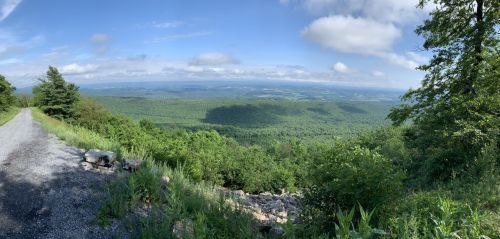 A panoramic view of lush green mountains under a partly cloudy sky, with a gravel path in the foreground.