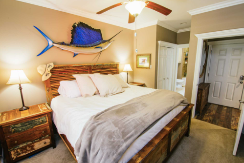 Cozy bedroom with a wooden bed, decorative fish on the wall, lamps, and a doorway leading to a bathroom.