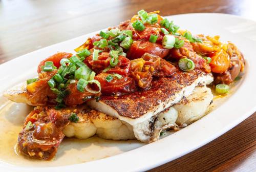 A plate of grilled fish topped with a vibrant tomato and green onion salsa, served on a bed of mashed potatoes.