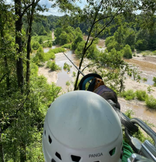 A view from above showing a zip line over a river surrounded by lush greenery and trees.