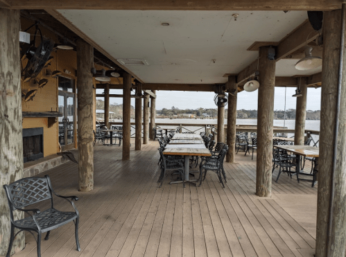 A spacious outdoor dining area with wooden pillars, tables, and chairs overlooking a calm water view.