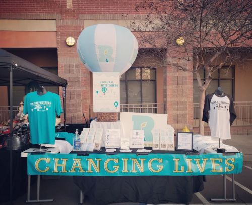 A booth display featuring merchandise and a hot air balloon decoration, promoting "Changing Lives" at an event.
