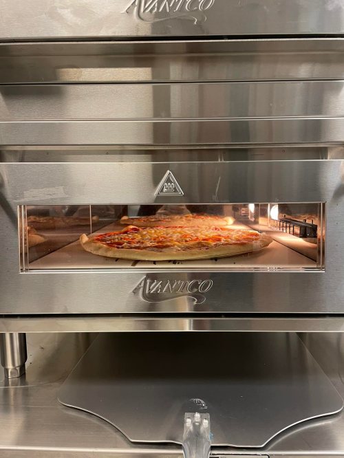 A pizza baking in a commercial oven with a stainless steel exterior and a glass viewing window.