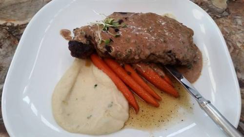 A plate featuring a steak with creamy sauce, served with carrots and a smooth puree, garnished with microgreens.