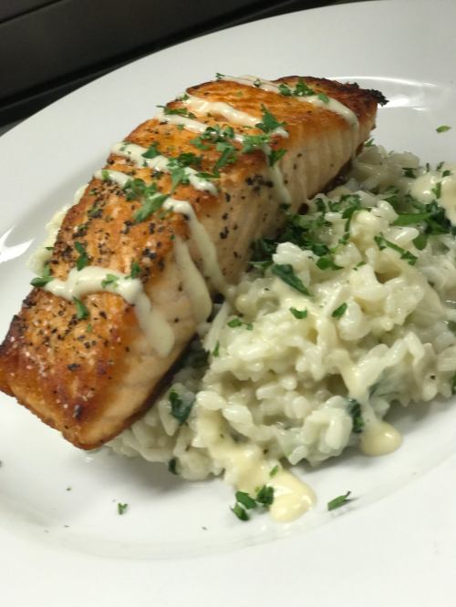 Grilled salmon fillet on a bed of creamy risotto, garnished with herbs and drizzled with sauce.